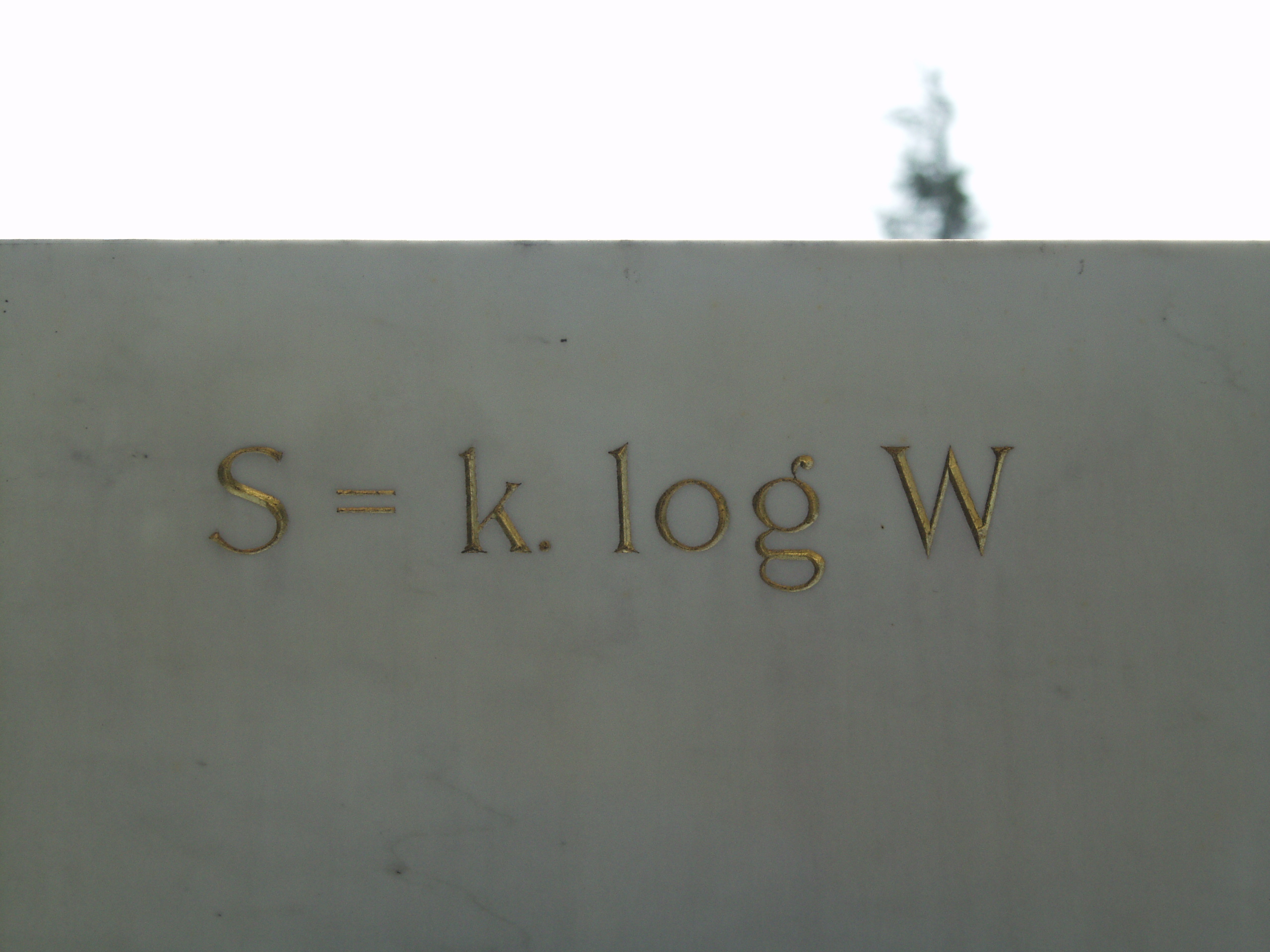 Vienna, Austria. Boltzmann's Tomb in the Zentralfriedhof (Central Cemetary). The Tomb is in Gruppe 14 C Grab No 1 (group 14 grave number 1). Photos by Tom Schneider or of him by Gerd Muller. 2002 July 14. This image: The famous engravement on the Tomb: S = k. log W. <a href = 